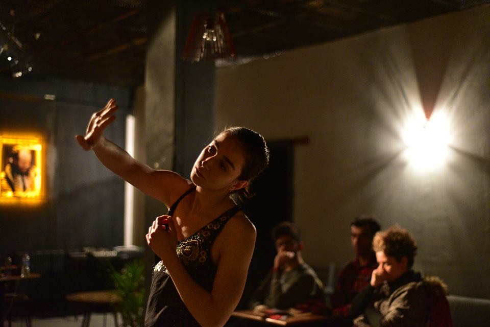 A dancer improvising in a lit room with a small audience watching.